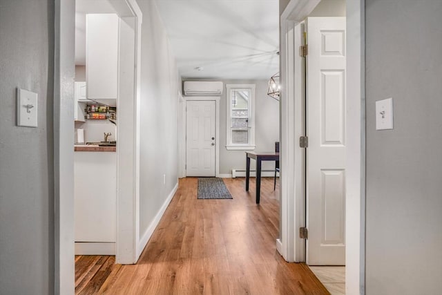 hall featuring a baseboard heating unit, light hardwood / wood-style floors, and a wall mounted AC