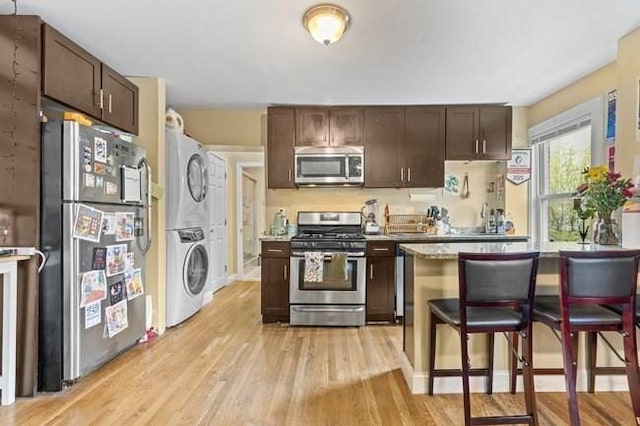 kitchen featuring appliances with stainless steel finishes, stacked washer / drying machine, dark brown cabinets, and light wood-type flooring