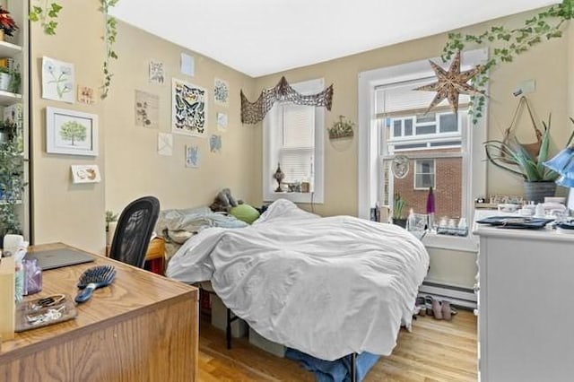 bedroom with a baseboard heating unit, light wood-style floors, and a desk