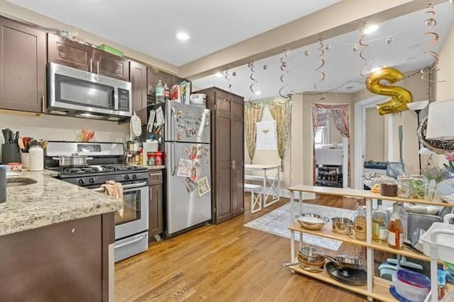 kitchen with appliances with stainless steel finishes, dark brown cabinetry, light wood-style flooring, and light stone countertops