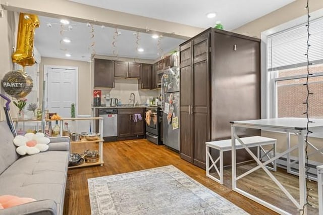 kitchen featuring appliances with stainless steel finishes, dark brown cabinets, a sink, and light wood-style floors