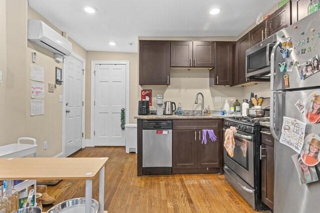 kitchen featuring appliances with stainless steel finishes, a sink, a wall unit AC, dark brown cabinetry, and light wood-style floors