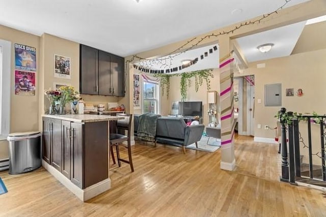 kitchen with light wood-style flooring, electric panel, light countertops, dark brown cabinetry, and open floor plan