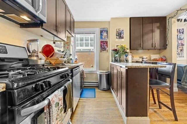 kitchen featuring stainless steel appliances, light wood-style floors, a breakfast bar area, and dark brown cabinets
