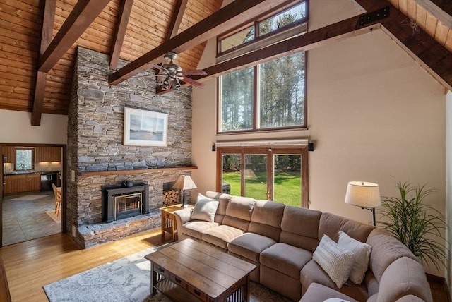 living room featuring wood ceiling, high vaulted ceiling, a stone fireplace, and beam ceiling