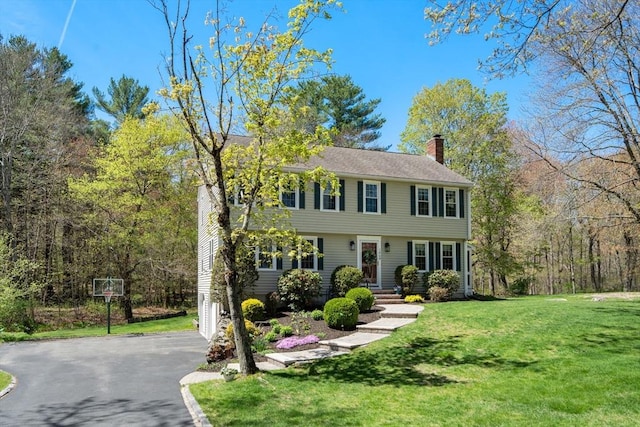 colonial inspired home with a chimney, a front yard, and aphalt driveway