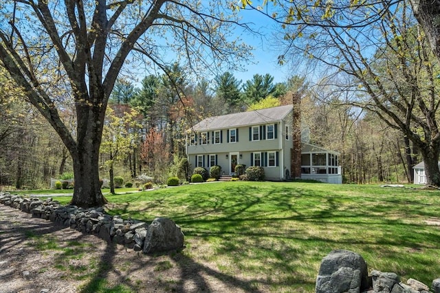 colonial home with a chimney, an outbuilding, a sunroom, a front yard, and a storage unit