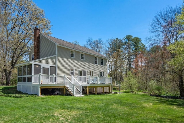 back of property featuring a sunroom, a chimney, a wooden deck, a yard, and stairs