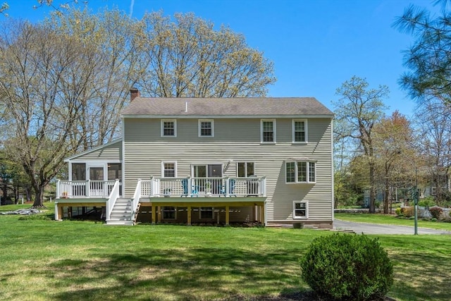 rear view of house with a yard, a wooden deck, a sunroom, and a chimney