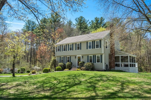 colonial house featuring a chimney, a front yard, and a sunroom
