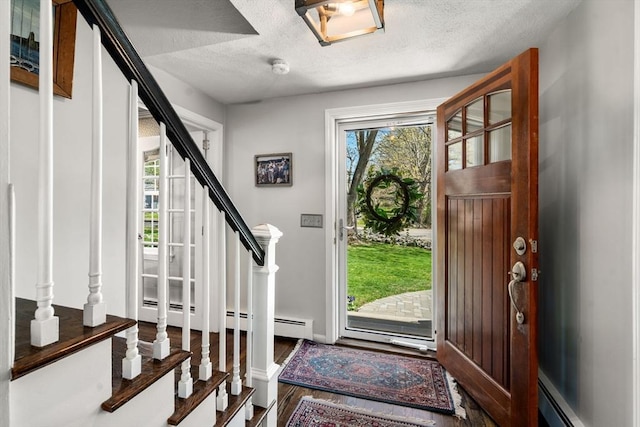foyer with a textured ceiling, stairway, wood finished floors, and a baseboard radiator