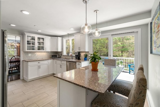 kitchen featuring a sink, stainless steel appliances, pendant lighting, white cabinets, and backsplash