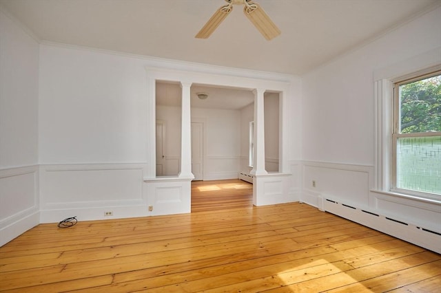 empty room with decorative columns, a baseboard heating unit, ceiling fan, light wood-style floors, and wainscoting