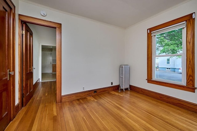unfurnished room featuring radiator heating unit, crown molding, hardwood / wood-style flooring, baseboards, and a smoke detector
