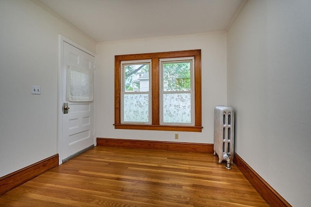 doorway to outside with radiator heating unit, wood finished floors, baseboards, and crown molding