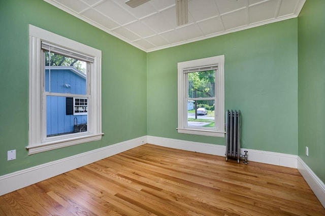spare room with radiator, baseboards, wood finished floors, crown molding, and a ceiling fan