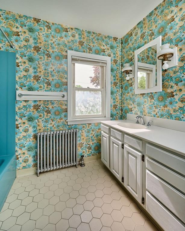 bathroom featuring radiator heating unit, wallpapered walls, baseboards, vanity, and a tub