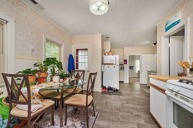 dining room featuring wallpapered walls, ornamental molding, and a wainscoted wall