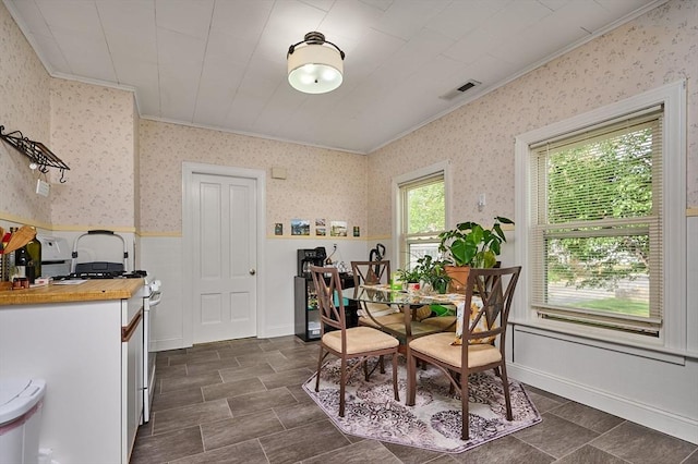 dining room with ornamental molding, wallpapered walls, and a wainscoted wall