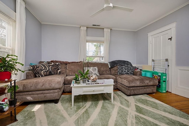 living room with wood finished floors, crown molding, ceiling fan, and a wainscoted wall