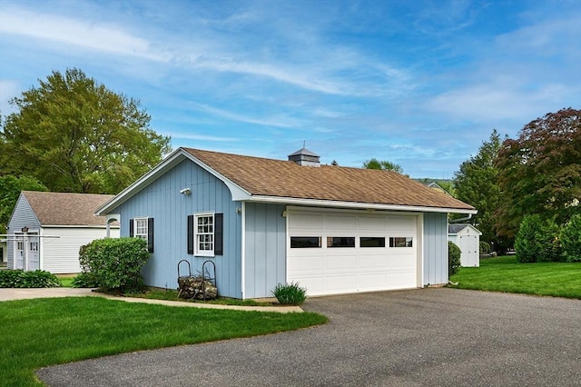 view of front of house with a garage, an outbuilding, a front yard, and roof with shingles