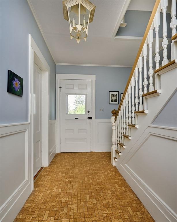 foyer entrance featuring a chandelier, a wainscoted wall, stairs, crown molding, and a decorative wall