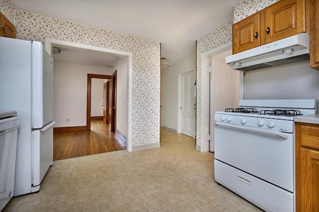 kitchen with white appliances, under cabinet range hood, brown cabinetry, baseboards, and light countertops