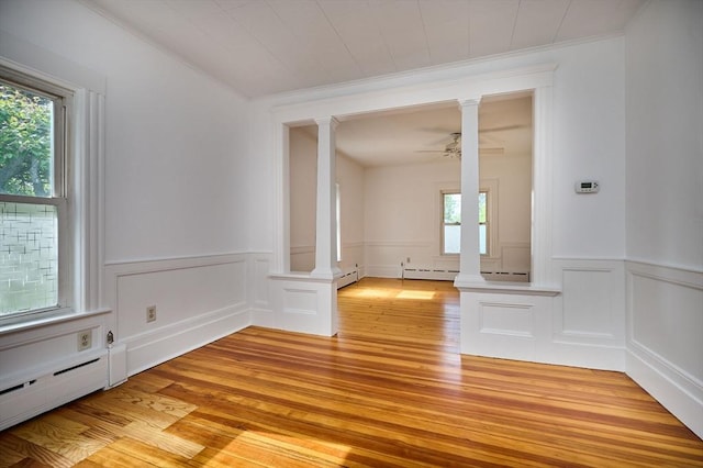 empty room featuring decorative columns, light wood-type flooring, healthy amount of natural light, crown molding, and a wainscoted wall