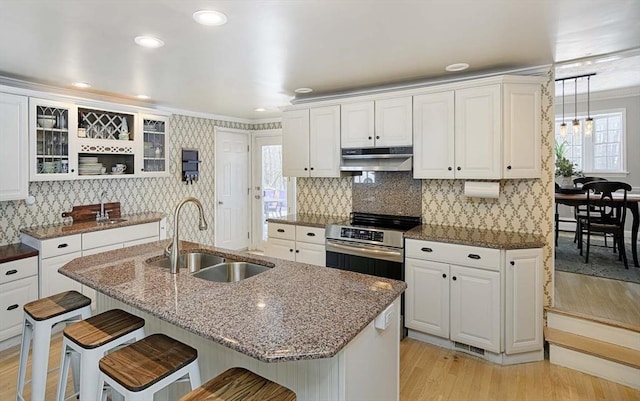 kitchen featuring under cabinet range hood, white cabinetry, a kitchen breakfast bar, and a sink