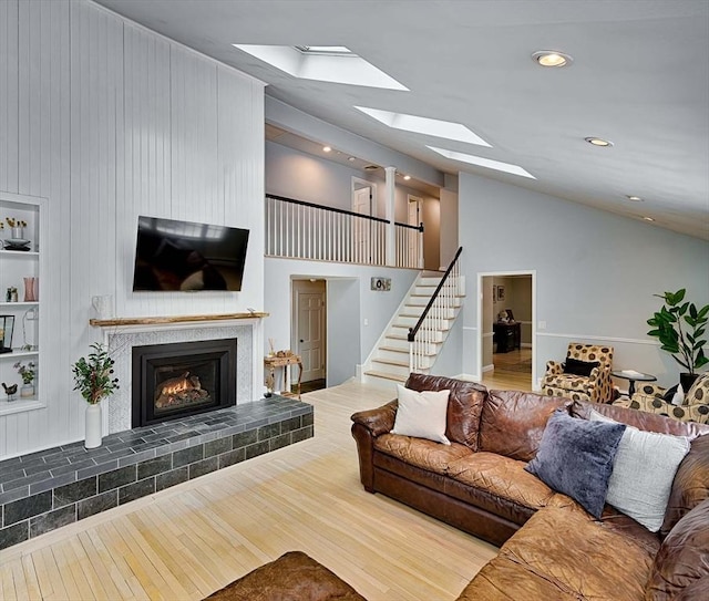 living room with a warm lit fireplace, vaulted ceiling with skylight, wood finished floors, stairs, and built in shelves