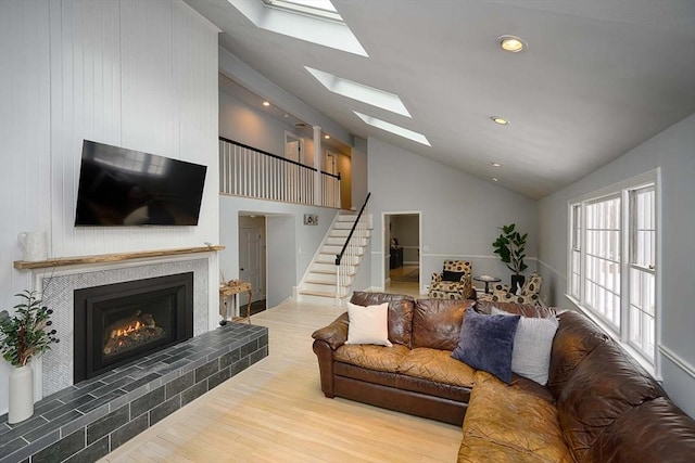 living room featuring vaulted ceiling with skylight, a tile fireplace, recessed lighting, wood finished floors, and stairs