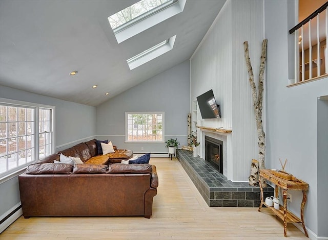 living area with a skylight, a baseboard heating unit, wood finished floors, and a glass covered fireplace