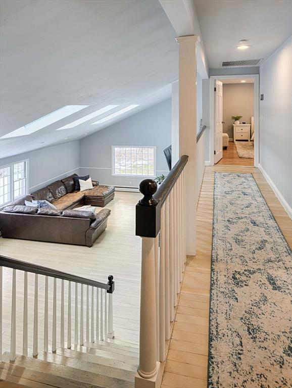 hall featuring visible vents, lofted ceiling with skylight, a wealth of natural light, and light wood-style floors