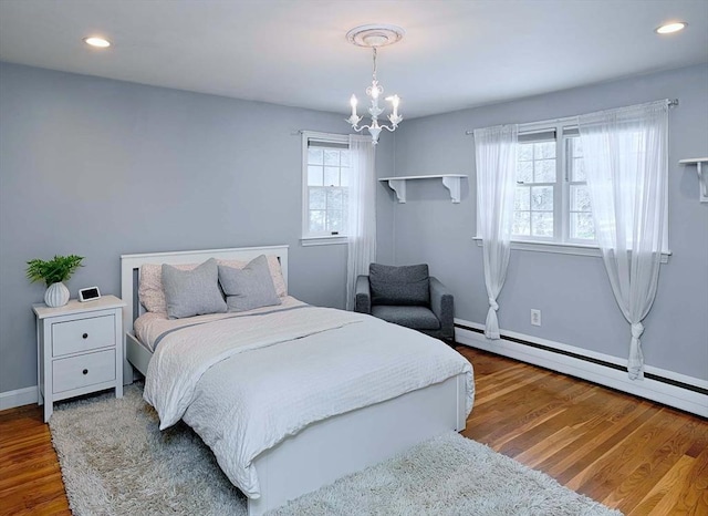 bedroom with a chandelier, baseboard heating, wood finished floors, and recessed lighting