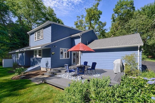 back of house with a deck, a lawn, and roof with shingles