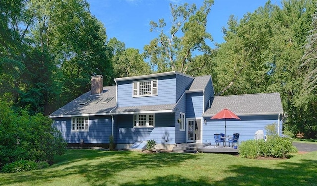 view of front facade with a shingled roof, a front yard, a chimney, and a wooden deck