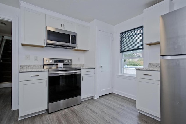 kitchen with appliances with stainless steel finishes, light wood finished floors, white cabinetry, light stone counters, and baseboards