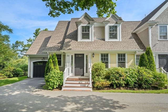 new england style home featuring a garage, aphalt driveway, and roof with shingles