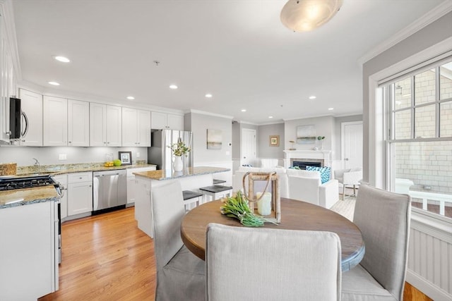 dining area featuring light wood-style floors, a fireplace, ornamental molding, and recessed lighting