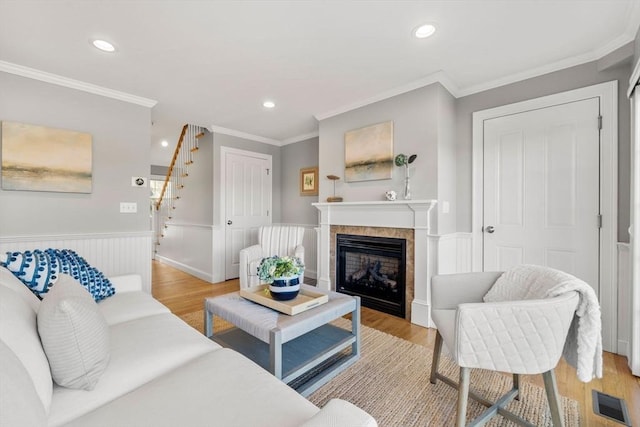 living room featuring light wood-type flooring, wainscoting, visible vents, and stairs