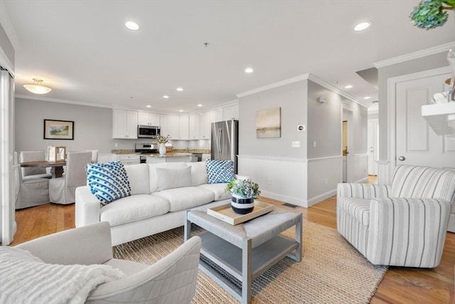 living room featuring ornamental molding, recessed lighting, wainscoting, and light wood-style floors