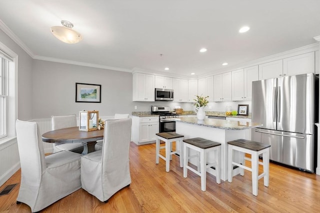 kitchen featuring white cabinets, appliances with stainless steel finishes, a center island, light stone countertops, and a kitchen bar