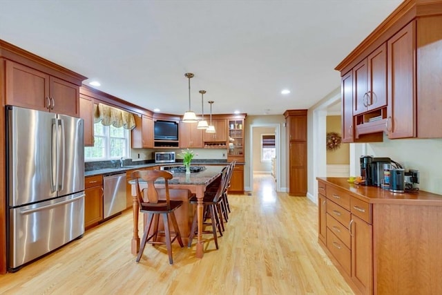 kitchen with stainless steel appliances, light wood-type flooring, a kitchen breakfast bar, pendant lighting, and a kitchen island