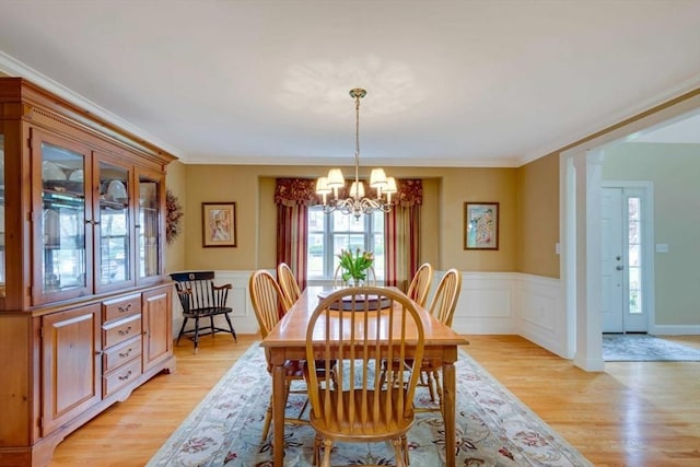 dining area featuring a chandelier, light wood-style floors, wainscoting, and ornamental molding