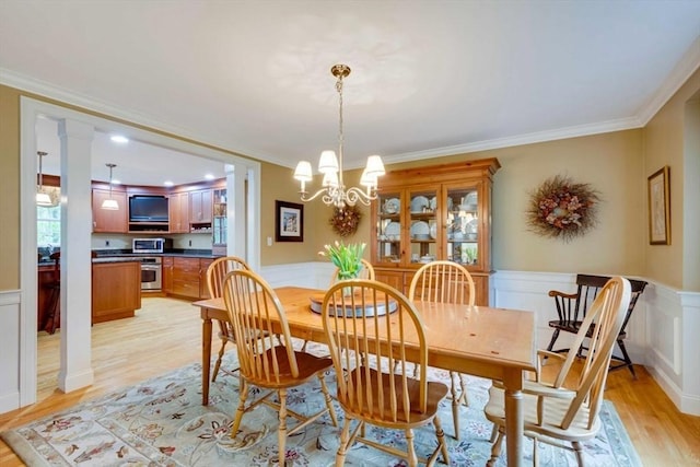 dining space with light wood finished floors, ornamental molding, wainscoting, a chandelier, and a decorative wall