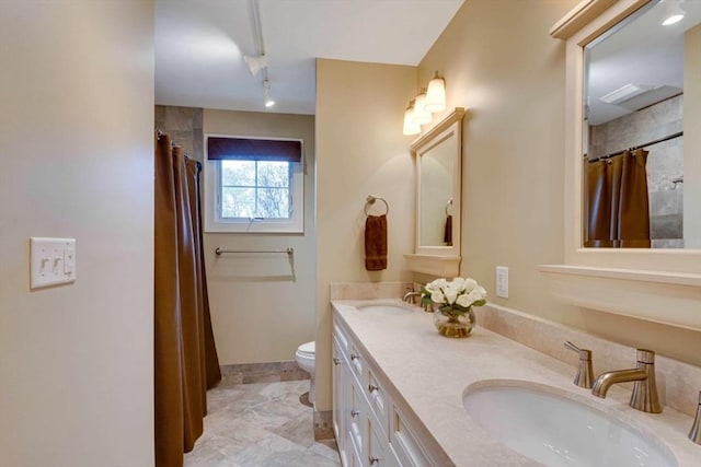 bathroom with toilet, double vanity, baseboards, rail lighting, and a shower with curtain