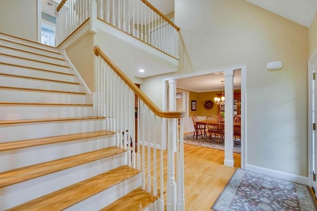 stairway with a towering ceiling, wood finished floors, ornate columns, a chandelier, and baseboards