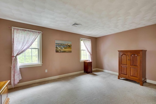 spare room featuring plenty of natural light, light carpet, and baseboards