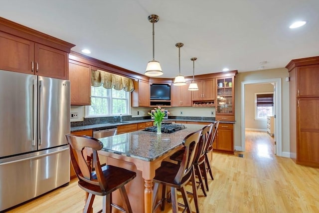 kitchen featuring stainless steel appliances, brown cabinetry, a sink, a breakfast bar, and light wood-type flooring