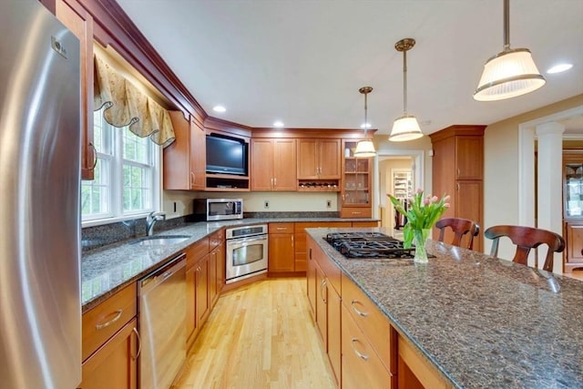 kitchen featuring appliances with stainless steel finishes, a sink, light wood-type flooring, hanging light fixtures, and dark stone countertops